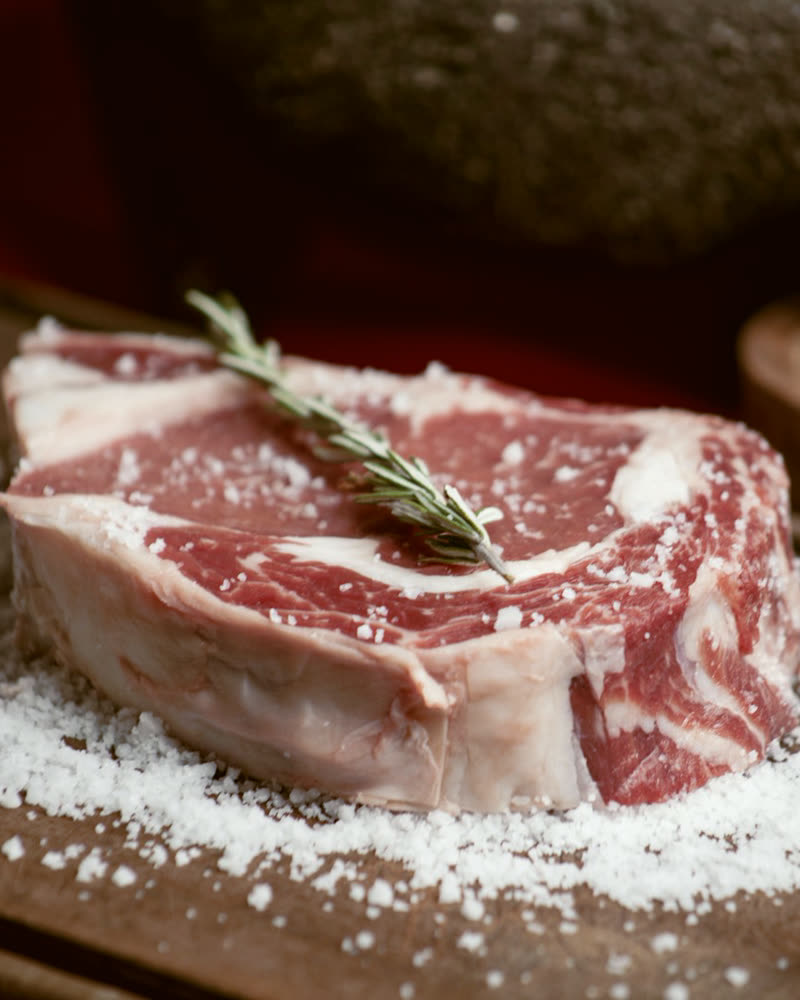 Raw tomahawk-cut steak on a wooden board with salt and rosemary